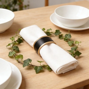 Detail of a matte black napkin ring with gold edges on a white linen napkin