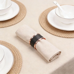 Detail of matte black napkin ring with rose gold metal edges on beige fabric napkin