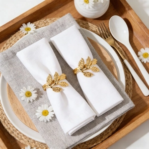 Golden leaf napkin rings set of two on white fabric over a minimalist wooden table