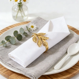 Golden mimosa leaf napkin ring with detailed metallic veins on white linen napkin