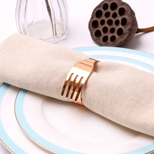 Detailed view of rose gold fork-shaped napkin ring on a beige linen napkin