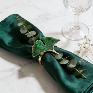Detail showing green enamel ginkgo leaf napkin ring with gold edges on silk fabric