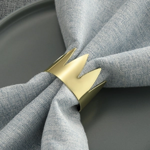 Detail eines mattgoldenen Kronen-Serviettenrings mit blauer Stoffserviette auf Tablett