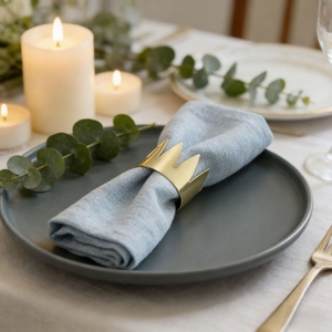 Eleganter goldener Serviettenring in Kronenform auf einer hellblauen Leinenserviette