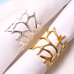 Detailed close-up of gold and silver coral branch napkin rings on white fabric linens