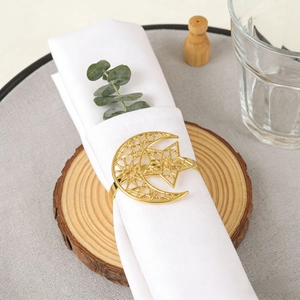 Golden hollow star and moon napkin ring on white fabric for elegant table setting