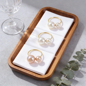Elegante goldene Serviettenringe mit weißen und Champagner-Perlen auf Holztablett