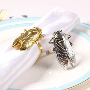 Golden and silver cicada shaped metal napkin rings shown on white fabric in a luxury setting