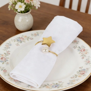 Detail of a gold star and pearl napkin ring on a white napkin over a floral plate
