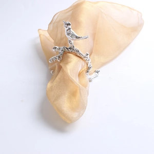 Detailed view of a silver bird napkin ring with realistic branch textures and gold fabric