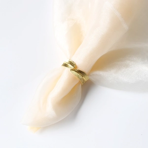 Close-up of golden leaf napkin ring with fine engraved texture on white silk fabric