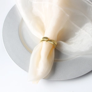 Detail shot of golden feather napkin ring with intricate texture on a beige fabric