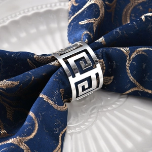 Silver Greek Key metal napkin ring on navy blue linen over a white ceramic plate