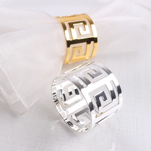 Detailed shot of gold and silver hollow Greek key pattern metal napkin rings on fabric