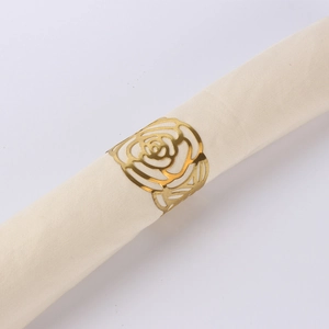 Detail of a golden rose napkin ring encircling a cream fabric napkin on a grey background