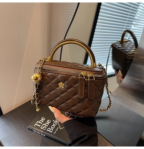 Detail of brown quilted camera bag featuring golden flower logo and metal handle