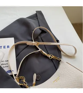 Detail of cream woven shoulder bag featuring adjustable strap and gold metal chain hardware