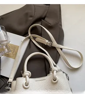 Detailed macro view of white pebble leather texture and metallic hardware on a small square bag