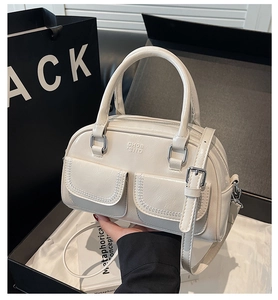 Close-up of white boston handbag with wavy stitching and logo in a black gift box