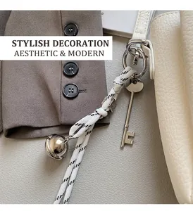 Detail of woven black and white strap with metal bell and key charm on white leather bag