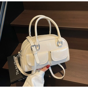 Detail shot of a cream leather Boston bag featuring dual front pockets on wooden stairs