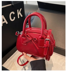 Detail of red glossy bow handbag with silver hardware and adjustable shoulder strap