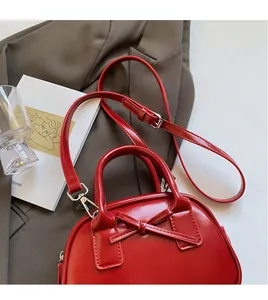 Detail view of red glossy crossbody bag with bow decoration on a brown blazer background