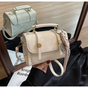 Close-up of a cream crossbody bag with glossy crackle texture and floral scarf detail