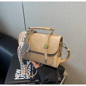 Dettaglio borsa a tracolla beige opaca con fibbia dorata e ciondolo intrecciato chic