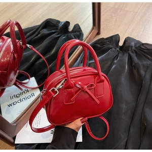 Detail of red patent leather bow bag with glossy finish and detachable shoulder strap