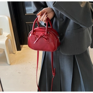 Detail of red faux leather bow handbag held by model with adjustable shoulder strap