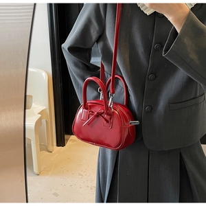 Close-up of bright red patent leather handbag with bow detail and silver zipper