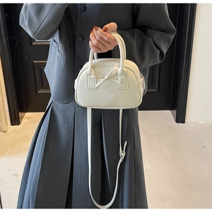Detail of elegant cream handbag featuring a chic bow and adjustable leather shoulder strap