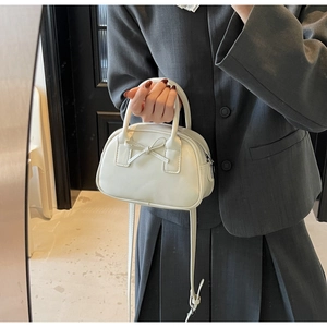Detailed view of white mini bowling bag with bow detail held by model in grey suit