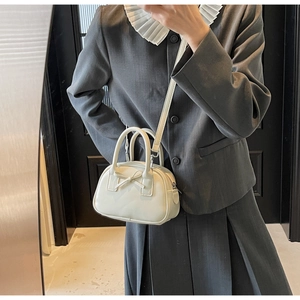 Detail of a creamy white mini handbag with a decorative bow and dual carry handles