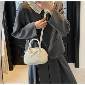 Chic cream bow shoulder bag on model with elegant grey suit in modern indoor setting