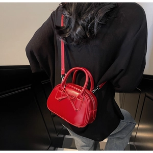Detail of red mini crossbody bag with bow accent worn over a black outfit by a model