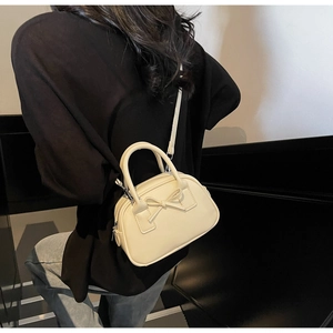 Detail of cream white mini bow bowling bag showing the adjustable shoulder strap and top handles