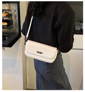 Close-up of cream rectangular shoulder bag with metal twist lock on a black blazer