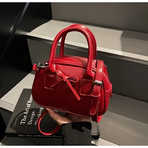 Detail of red glossy mini Boston bag with bow accent and silver adjustable strap