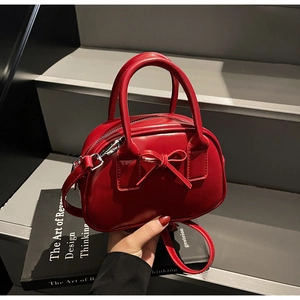 Detailed view of red glossy mini bowling bag with bow on a black book background