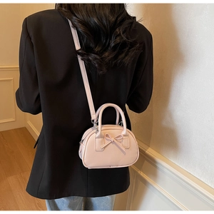 Close-up of pink mini crossbody bag with bow detail on black suit for size reference