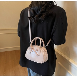 Crossbody pink bowling bag with bow detail worn by a model in a black suit