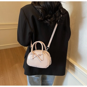 Detail of pink bow-knot crossbody bag shown on a model in a minimal interior setting