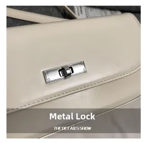 Detailed close-up of a silver metal swivel lock on an off-white leather shoulder bag