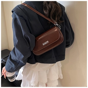 Detail of dark brown glossy leather underarm bag with silver twist lock on female model