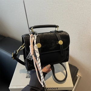 Retro matte black handbag with gold hardware and woven pendant in a handheld pose