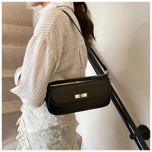 Close-up of a black minimalist baguette bag with a silver rotating metal lock and strap