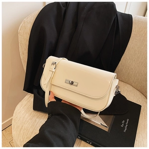Detail of a creamy beige leather baguette bag with a silver swivel lock on a woven chair