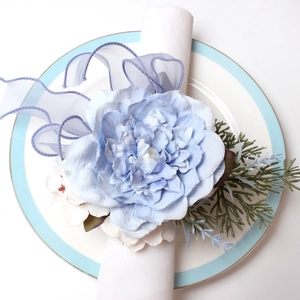 Detail of light blue sunflower napkin ring with pearl and ribbon on a ceramic plate